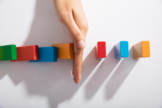 Close-up Of Businessperson Hand Stopping Colorful Blocks From Falling On Table In Office